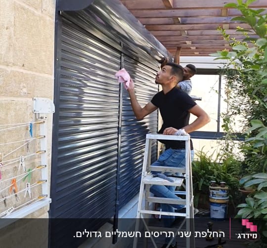 אדם מנקה תריסים עם מטלית ורודה על סולם
